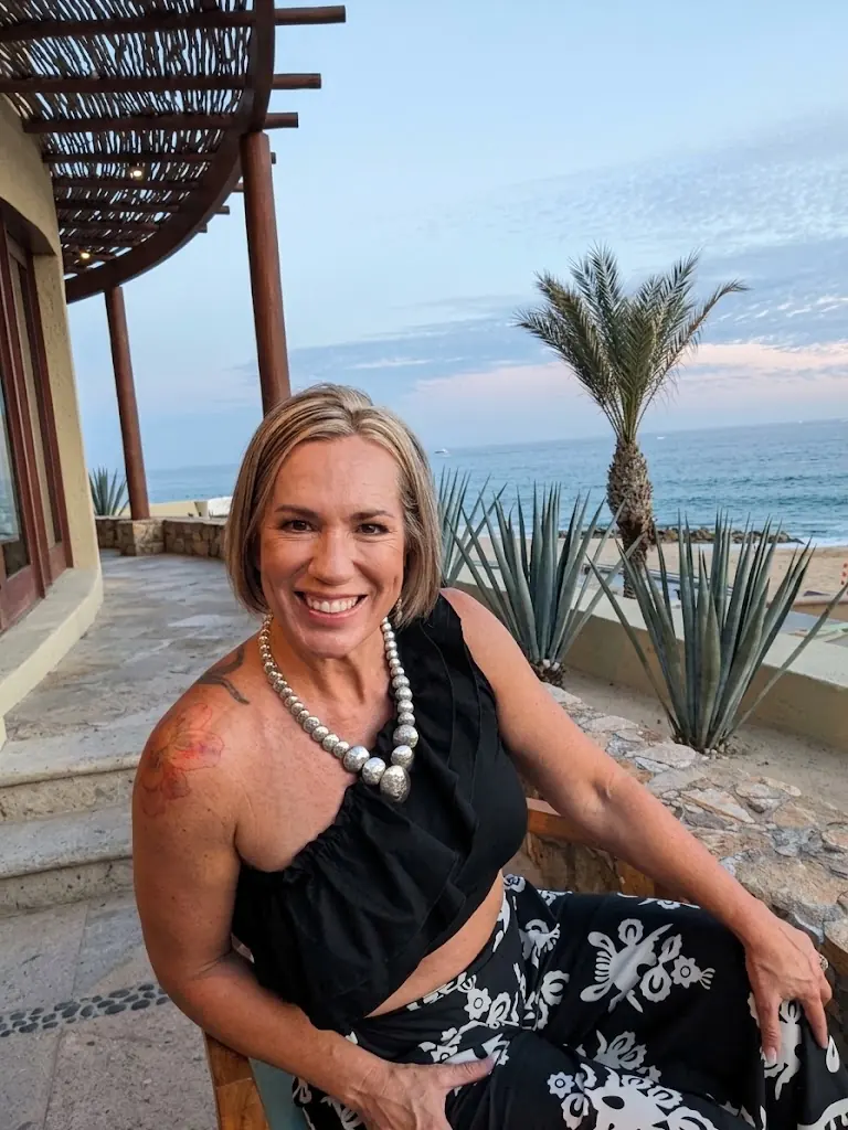 Jill McCracken smiling, seated on a terrace by the ocean at sunset