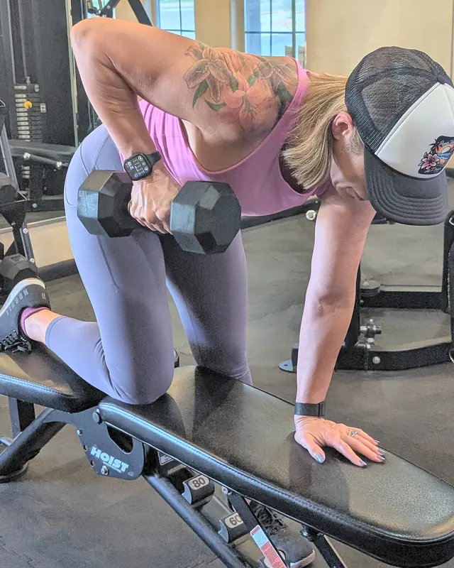 Jill doing a one-arm dumbbell row with one knee and hand on a bench