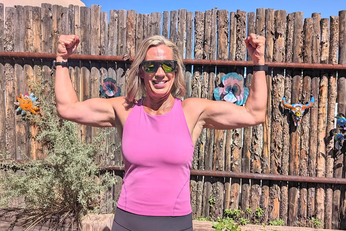 Jill flexing both arms in her backyard in front of a wooden fence
