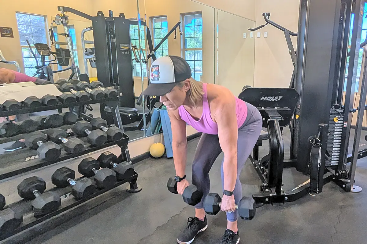 Jill doing a dumbbell Romanian deadlift at the gym, hips back and dumbbells close to her legs