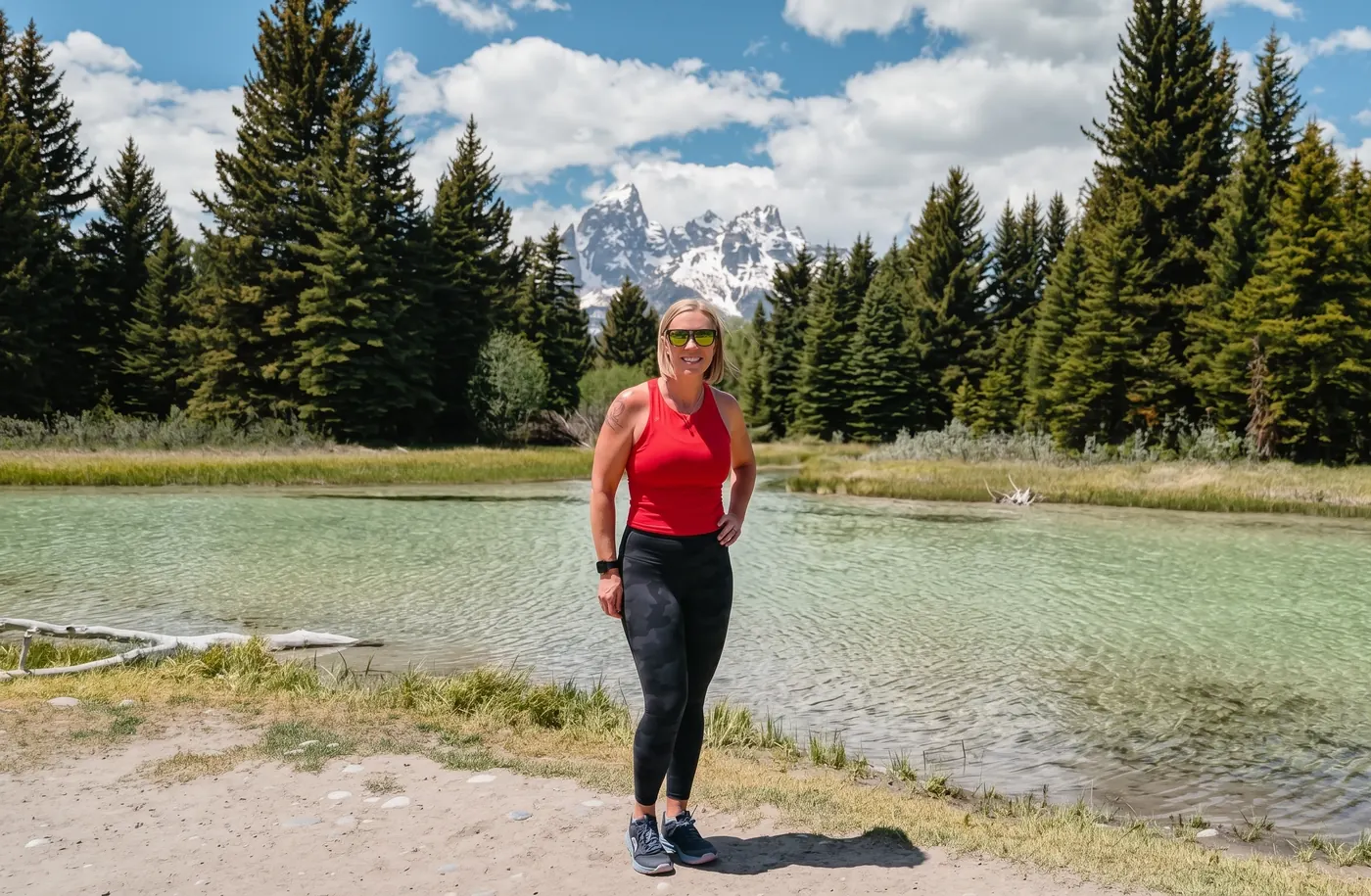 Jill standing by a clear river, with pine trees and snow-capped mountains behind her