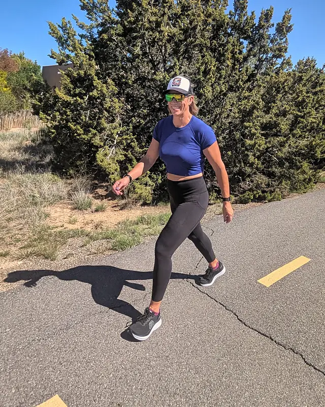 Jill smiling as she walks briskly on a paved trail on a sunny day