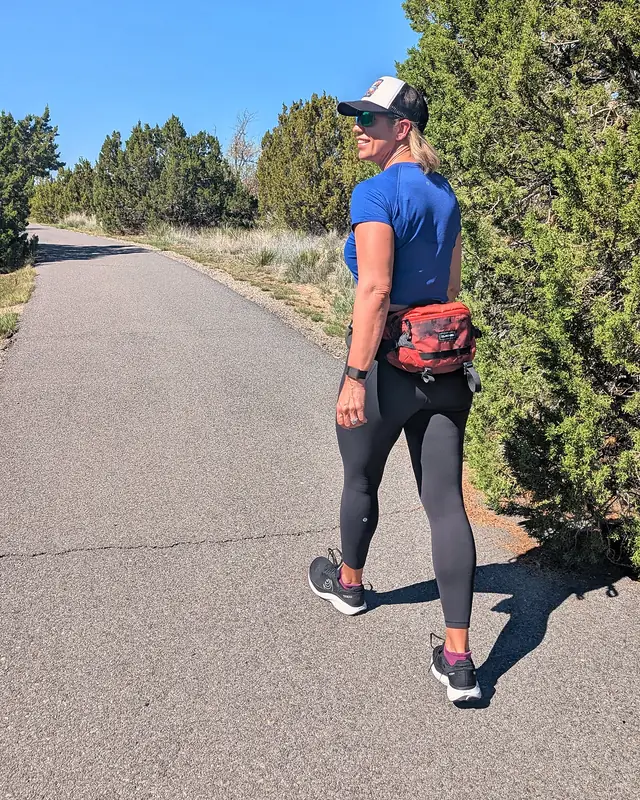 Jill walking on a paved trail between juniper trees, looking back and smiling